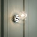Chrome wall light with an illuminated wire-filled glass globe mounted on a light green paneled wall.