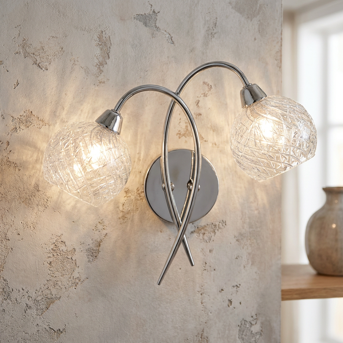 Oaks Tarn twin arm wall light in chrome with patterned glass shades on a rustic wall.