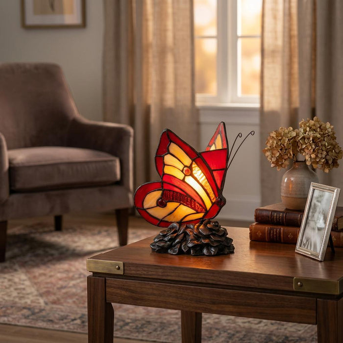 Stained glass butterfly table lamp with red and amber wings glowing on a wooden side table in a cozy living room.