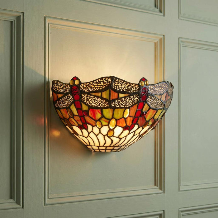 Lit Tiffany dragonfly wall lamp with red and amber stained glass on a light green paneled wall.