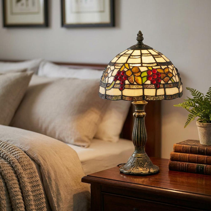 Oaks Tiffany Grapes Bedside Lamp with a stained glass grape motif shade glowing on a wooden nightstand.