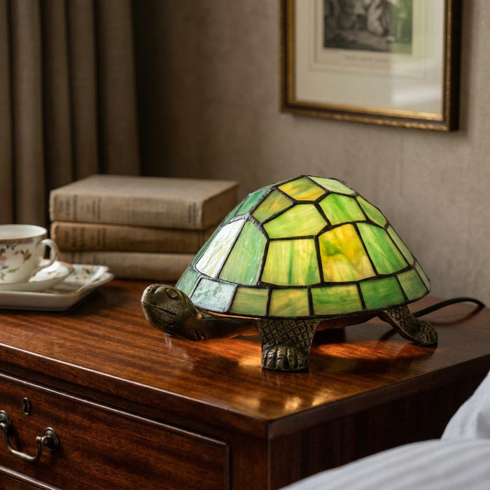 Tortoise table lamp with a green Tiffany-style glass shell sitting on a wooden bedside table.