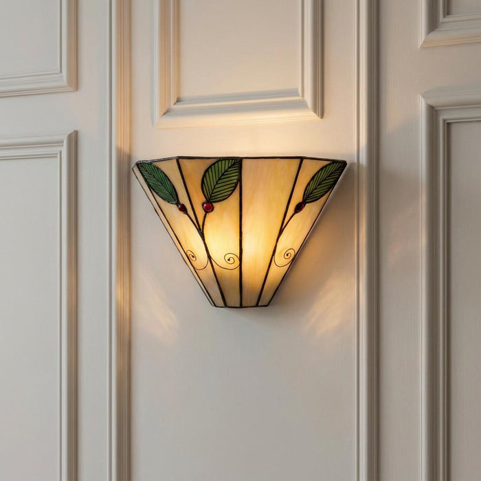 A Tiffany-style wall light with green leaf and red berry glass motifs mounted on a white panelled wall.