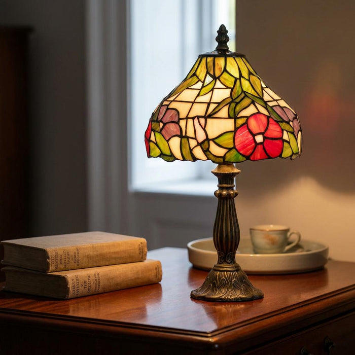 Tiffany lamp with a floral stained glass shade glowing on a wooden bedside table beside vintage books.