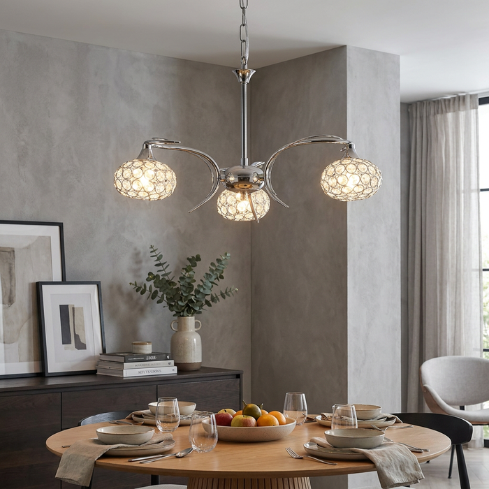 Modern three-light chrome chandelier with crystal-beaded shades over an elegant dining table setting.