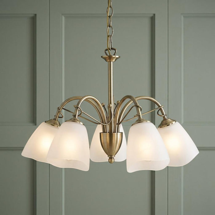 Oaks Turin 5 light antique brass chandelier with tulip frosted glass shades against a green paneled wall.