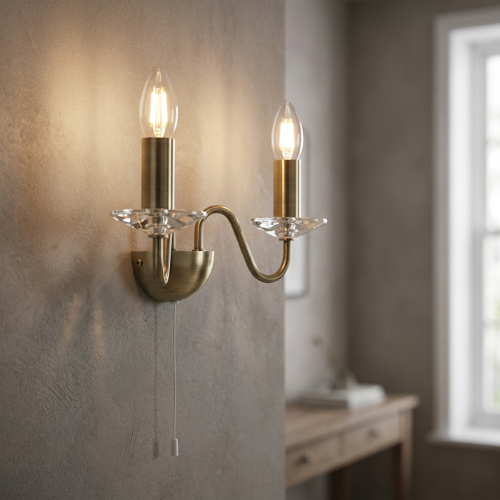 Oaks Vesta 2-light antique brass wall sconce with crystal dishes and pull cord switch on a neutral wall.