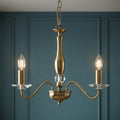 Three-light antique brass chandelier with crystal glass accents and candle-style bulbs against a teal paneled wall.