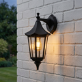 Black lantern-style outdoor wall light with a glowing bulb mounted on a white brick exterior wall.