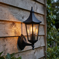 Black traditional lantern outdoor wall light illuminated on a rustic wooden fence.