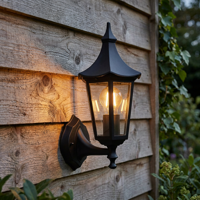Black traditional lantern outdoor wall light illuminated on a rustic wooden fence.