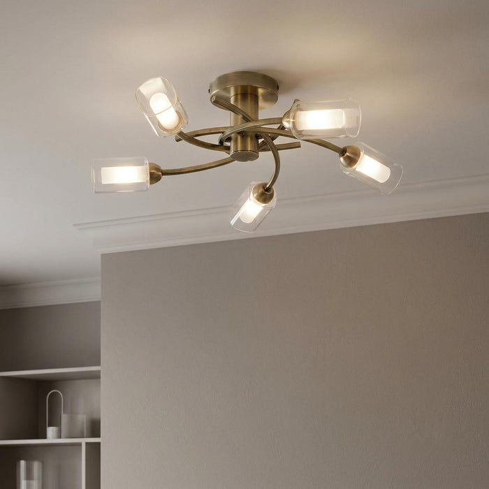 Antique brass flush ceiling light with five curved arms and clear glass cylinder shades.