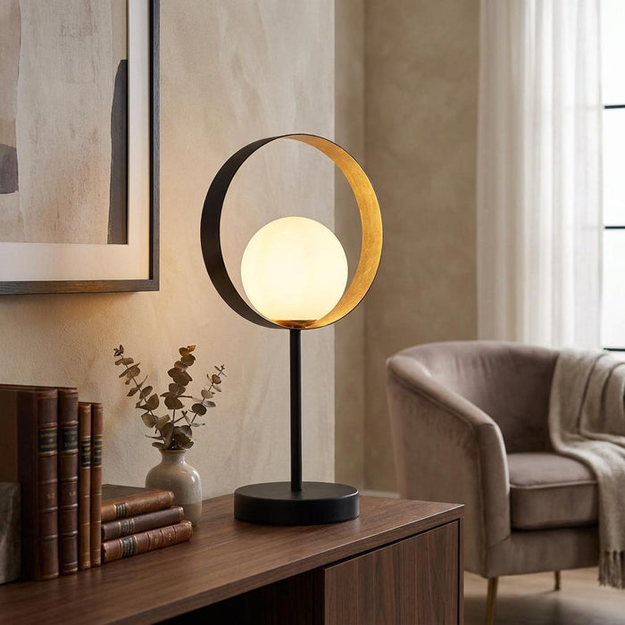 Matt black orbital table lamp with an opal glass globe on a wooden sideboard next to vintage books.