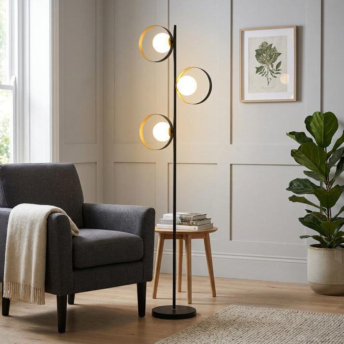 Modern black and gold floor lamp with three orbital globe lights in a contemporary living room setting.