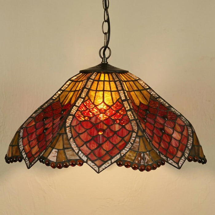 Hanging Tiffany pendant light with scalloped red and amber stained glass shade glowing against a wall.
