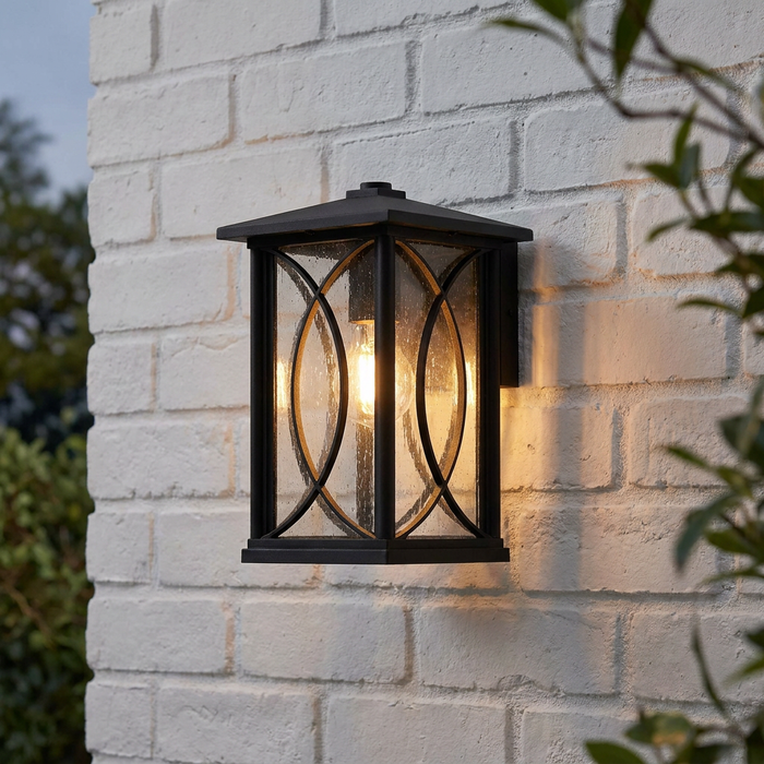 Lit Orton black outdoor wall lantern with bubble glass panels mounted on a white brick wall.