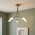 Five-light antique brass semi-flush ceiling light with cylinder shades, mounted against a sage green wall.