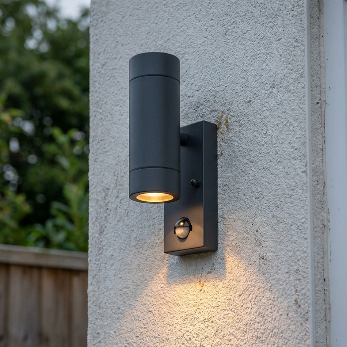 Modern grey cylindrical outdoor wall light with integrated PIR sensor mounted on a white textured wall.