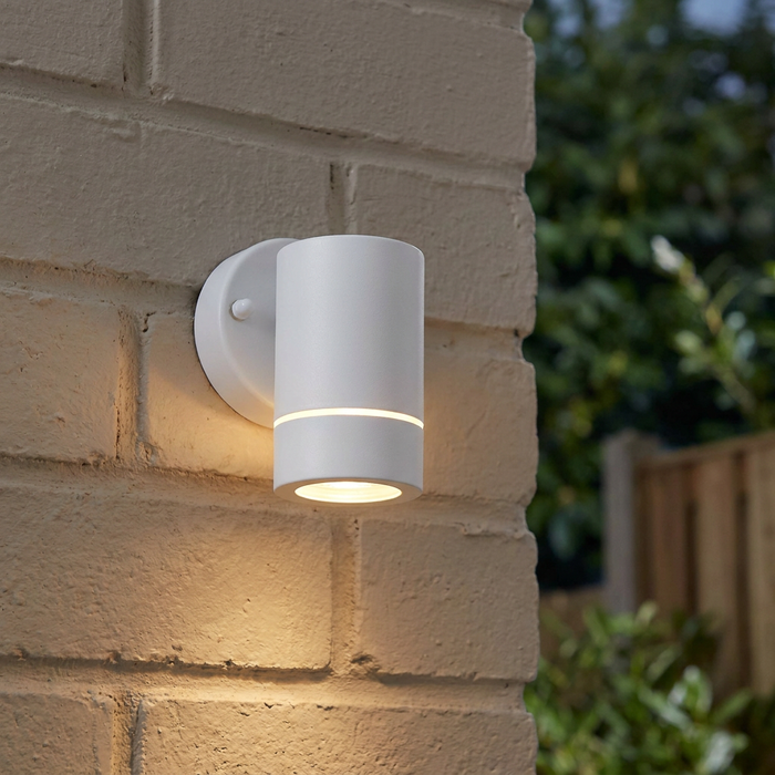Modern white cylindrical outdoor wall light mounted on a brick wall, illuminated with a downward glow.