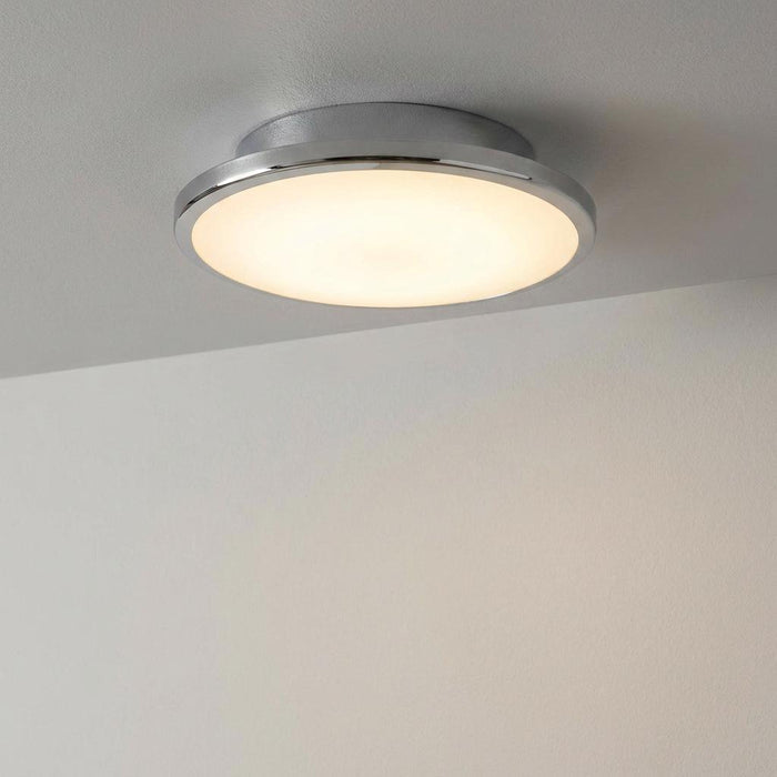 Circular chrome-rimmed flush ceiling light with a warm glow, mounted on a white ceiling.