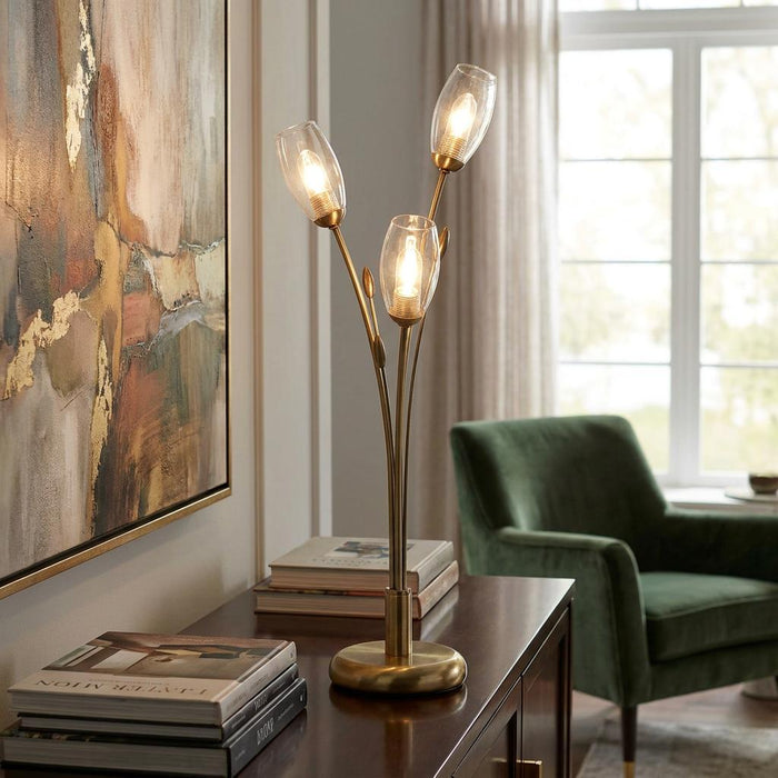 Antique brass table lamp with three branch-like stems and clear glass shades glowing on a wooden sideboard.