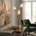 Antique brass table lamp with three branch-like stems and clear glass shades glowing on a wooden sideboard.
