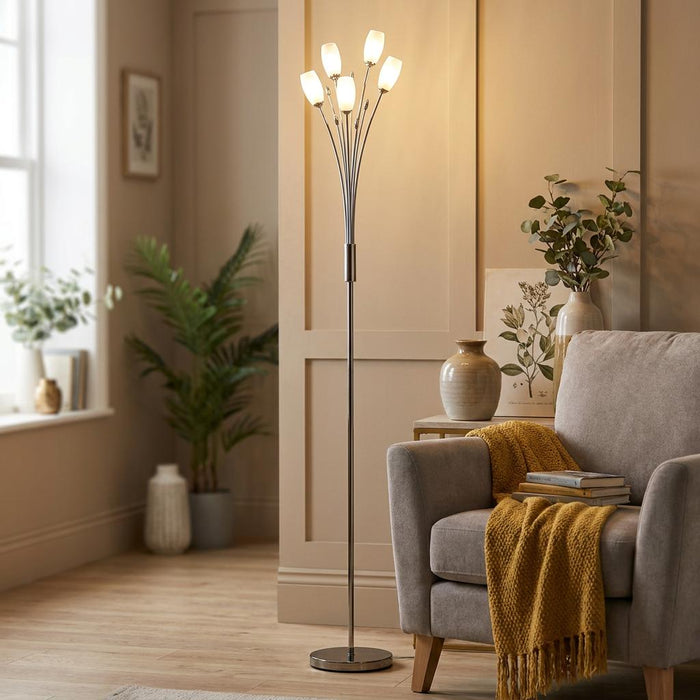 Five-light chrome floor lamp with glowing tulip shades next to an armchair in a modern living room.