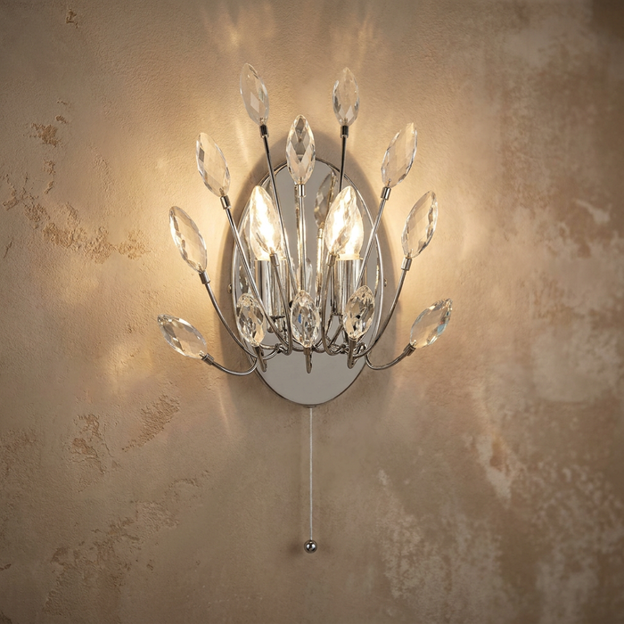 Peacock crystal and chrome 2-light wall sconce with a cord pull, illuminated against a textured beige wall.