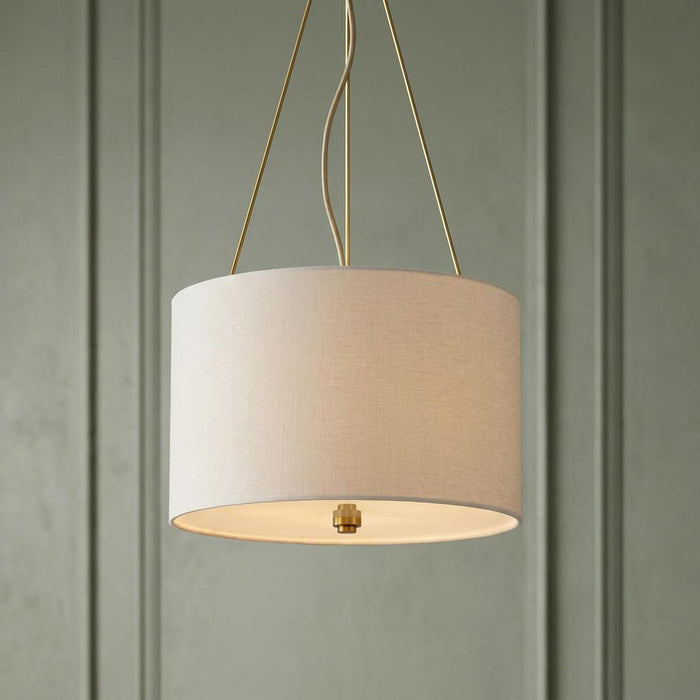 Cream linen drum pendant light with brass accents suspended in front of a sage green paneled wall.