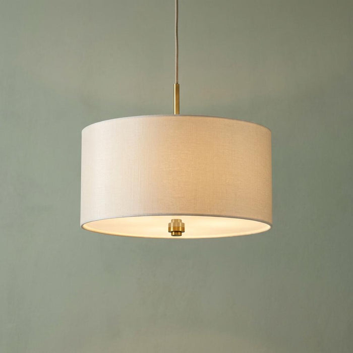 Pearce 18-inch pendant light with a linen drum shade and brass accents glowing against a sage green wall.