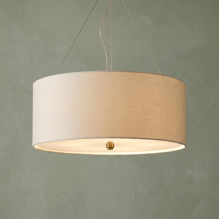 Cylindrical linen pendant light with brass detailing hanging from the ceiling.