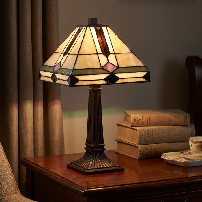Mission-style Tiffany table lamp with a geometric glass shade on a wooden table beside antique books.