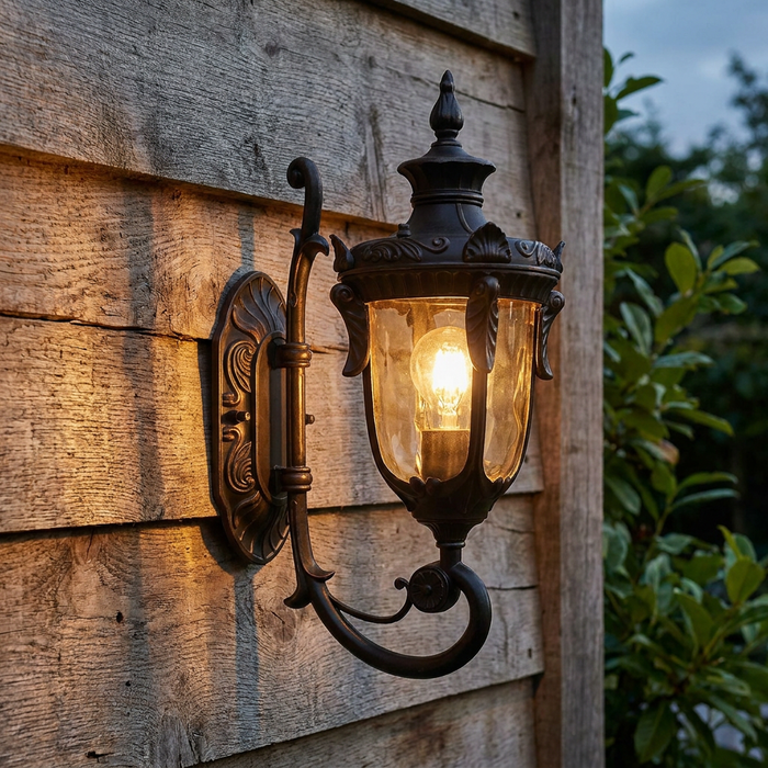 Traditional old bronze outdoor uplighter wall light with a glowing bulb mounted on a rustic wooden wall.