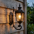 Traditional old bronze outdoor uplighter wall light with a glowing bulb mounted on a rustic wooden wall.