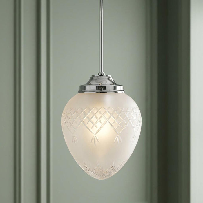 Frosted acorn-shaped pendant light with diamond-cut glass and chrome accents hanging against a green wall.