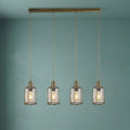 Four industrial brass pendant lights with seeded glass shades and wire cages against a muted teal wall.