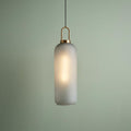 Pipette-shaped acid glass and brass pendant light glowing against a soft green wall.
