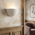 A white bowl-shaped plaster uplighter wall light casting a soft glow against a textured, rustic plaster wall.