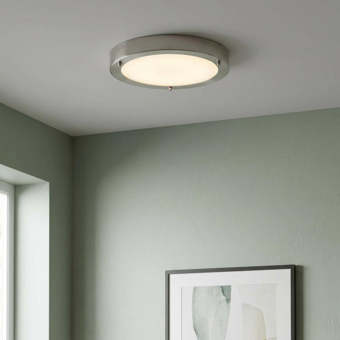 A circular nickel and glass flush LED ceiling light glowing on a white ceiling in a room with sage green walls.