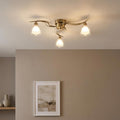 Portland 3-light antique brass flush ceiling fixture with wavy arms and frosted glass shades on a white ceiling.