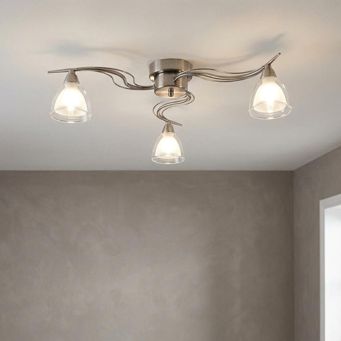 A three-light flush ceiling fixture with wavy antique chrome arms and clear glass bell shades on a white ceiling.