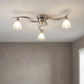 A three-light flush ceiling fixture with wavy antique chrome arms and clear glass bell shades on a white ceiling.