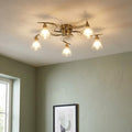 Five-light antique brass flush ceiling light with clear glass shades illuminated in a room with green walls.