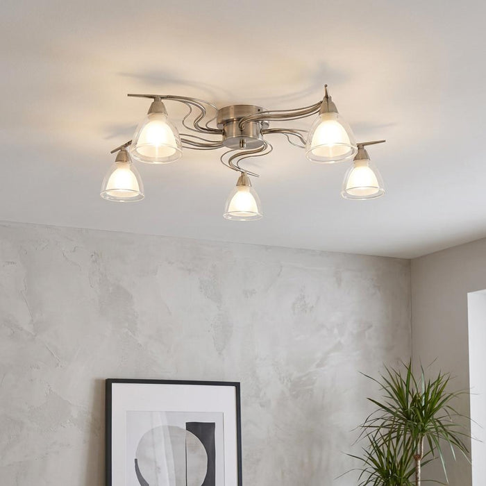5-light antique chrome flush ceiling light with wavy arms and frosted glass shades, illuminated in a modern room.