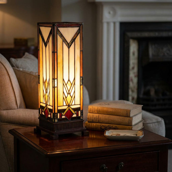 Lit Prairie Medium Tiffany Square Table Lamp with geometric stained glass on a wooden side table near books.