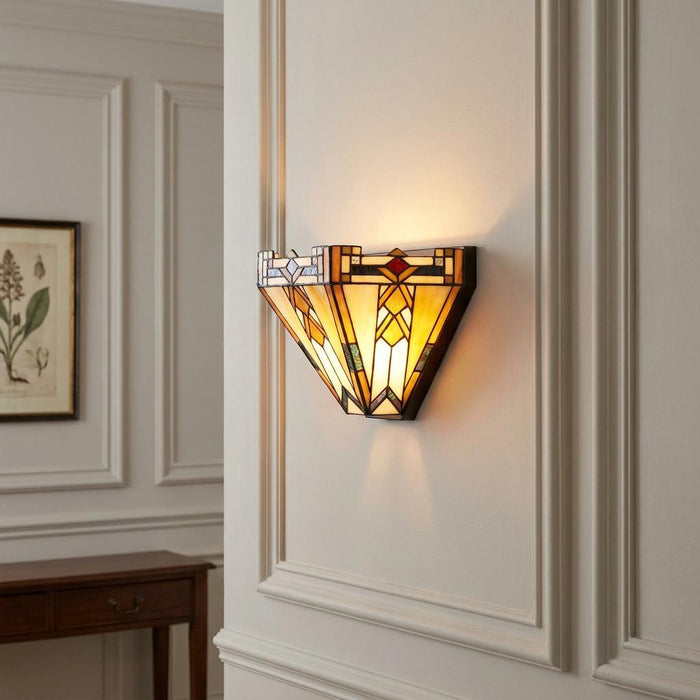 Lit Prairie-style Tiffany wall sconce with amber geometric glass mounted on a classic paneled cream wall.
