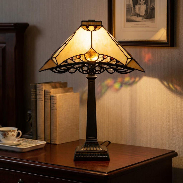 Priory Tiffany table lamp with an amber art glass shade and bronze base, sitting on a wooden sideboard with books.