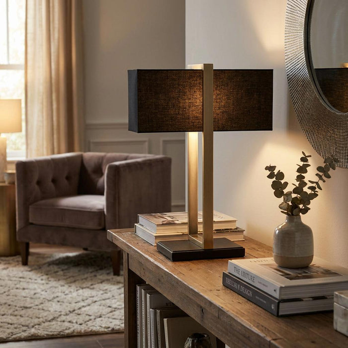 Produr brass table lamp with a black linen shade on a wooden console table in a warm living room.