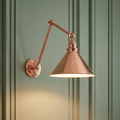Polished copper adjustable swing arm wall light with a conical shade mounted on a green paneled wall.