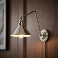 Polished nickel swing-arm wall light with a conical shade mounted on a dark wood-paneled wall.
